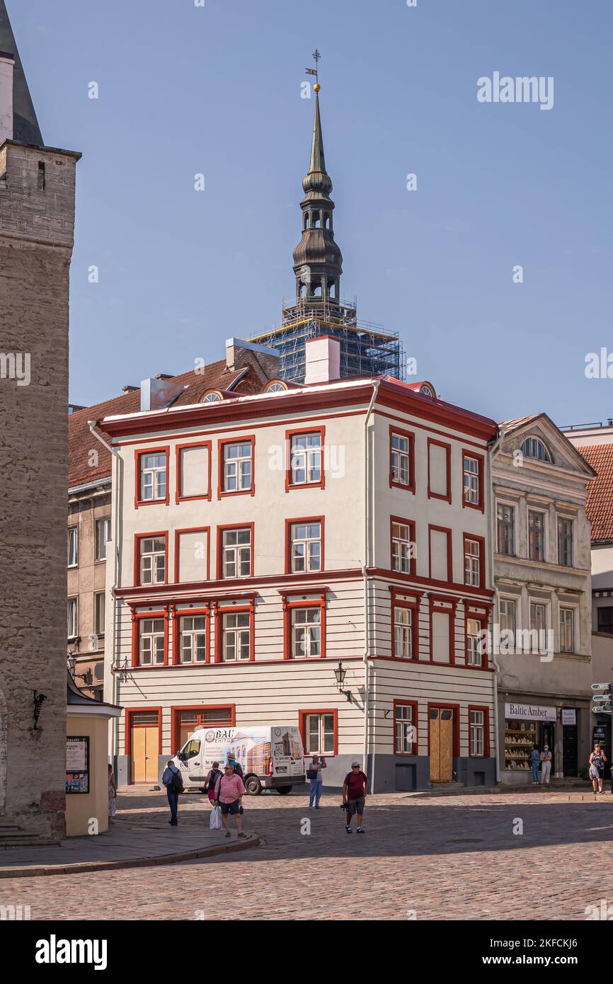 Estonia, Tallinn - 21 luglio 2022: Casa ristrutturata con facciata bianca e finestre rifilate rosse nell'angolo sud-ovest della Piazza del Municipio con guglia di San Nichola Foto Stock