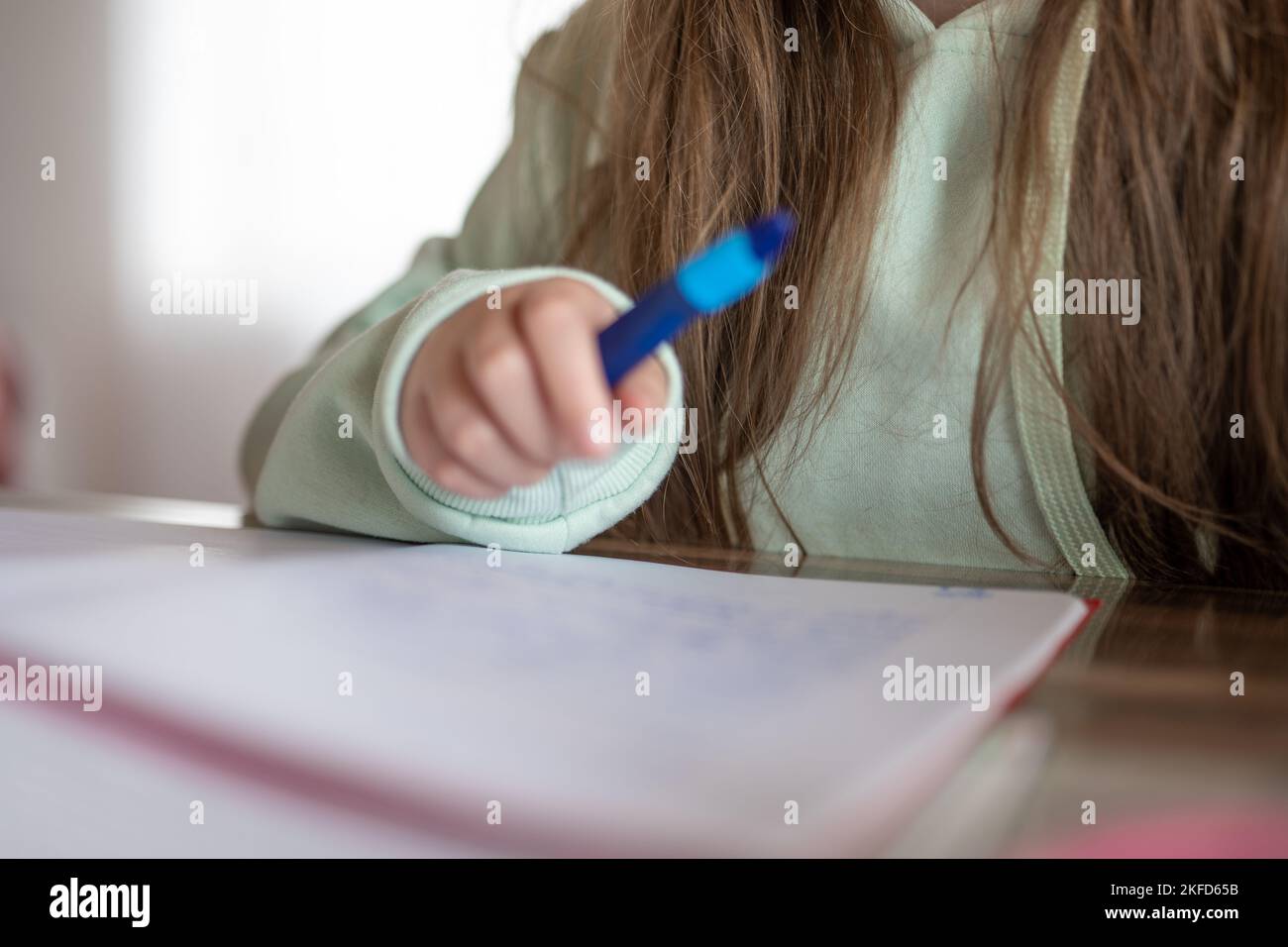 Homewwork.schoolgirl fa il suo lavoro. il bambino scrive con una matita in un taccuino. matita in una mano di bambini. Foto Stock