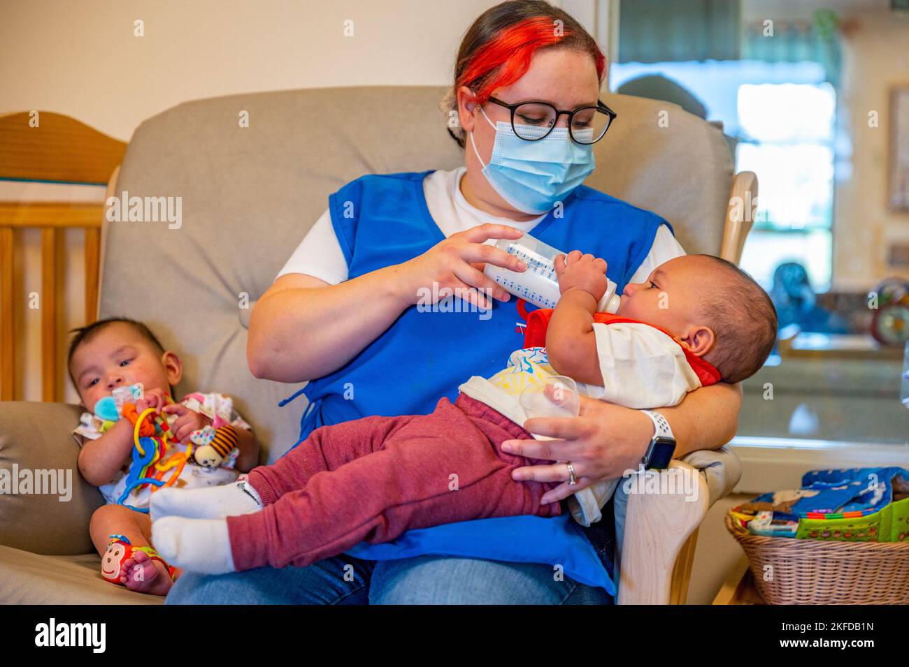 Un operaio del Malmstrom Child Development Center nutre un bambino mentre un altro gioca con i giocattoli il 8 settembre 2022 alla base dell'aeronautica militare di Malmstrom, Month. Il programma infantile del CDC è progettato per i bambini da sei settimane a 12 mesi. Il CDC fornisce assistenza ai bambini delle famiglie militari attive e del personale civile del DoD/NAF. Con un numero limitato di servizi di assistenza all'infanzia disponibili nello stato del Montana, il CDC è un servizio essenziale presso la Malmstrom AFB. Foto Stock