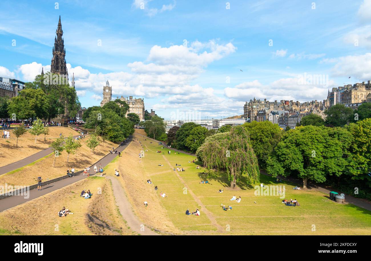 Edimburgo, Scozia, luglio 30 2022: Durante la stagione estiva del Fringe Festival, molte persone si siedono e si rilassano sull'erba baciata dal sole, vicino allo Scott Monument Foto Stock