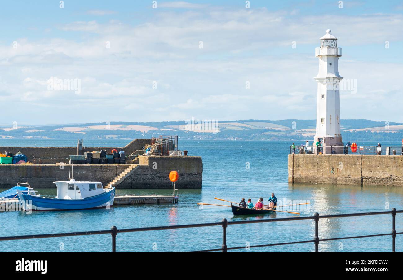 Edimburgo, Scozia-30 2022 luglio: Una piccola barca di legno di remi entra nel piccolo porto di pescatori, trasportando i viaggiatori della barca, galleggiando sulle acque tranquille e lisce, su un Foto Stock