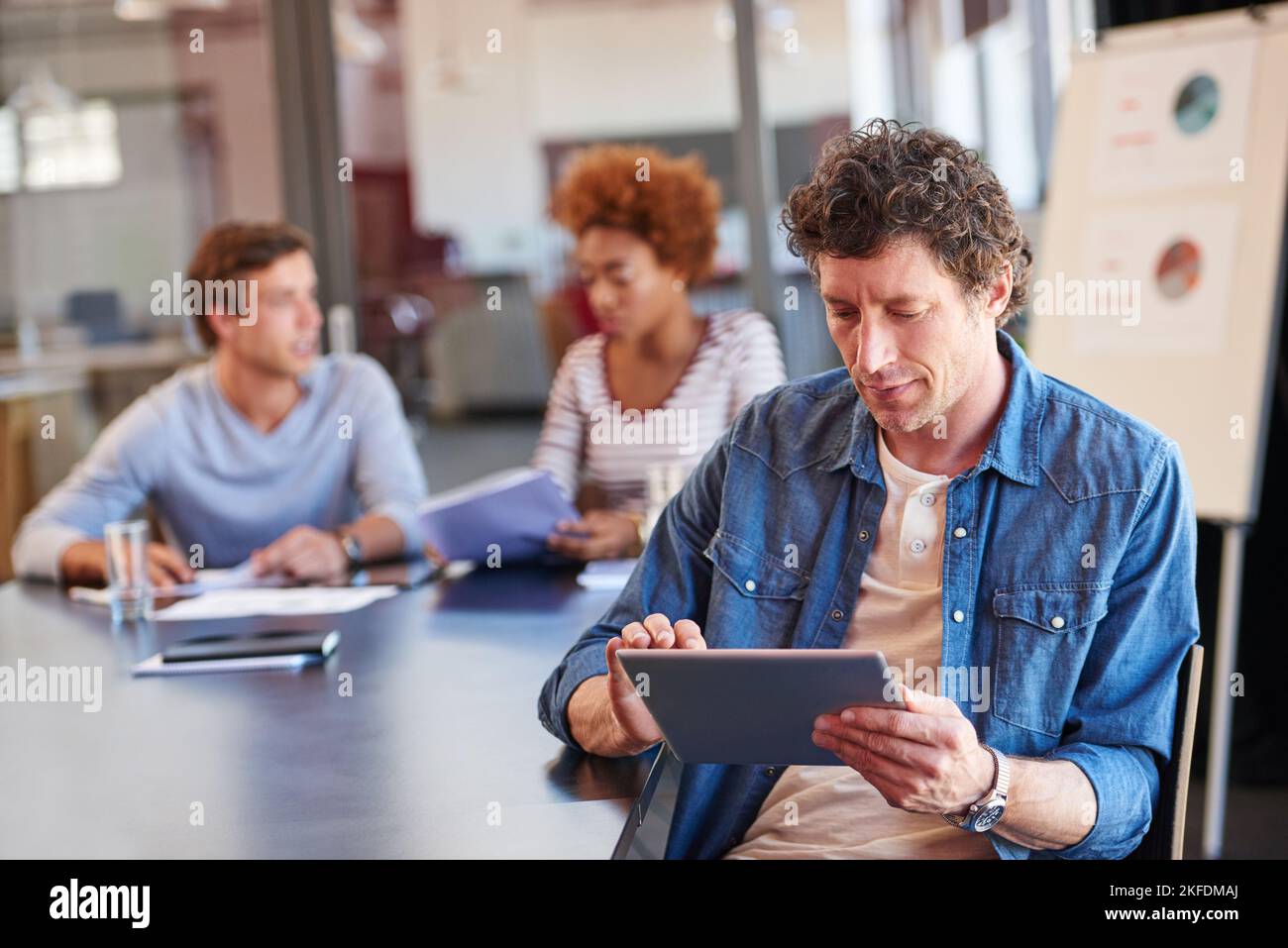 Informazioni facilmente accessibili durante la sessione di brainstorming. Immagine di un uomo che utilizza un tablet digitale in una sala riunioni con i suoi colleghi nella Foto Stock