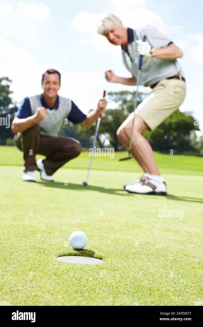 Sì. Due uomini eccitati sul verde durante una partita di golf guardando la palla rotolare nel buco. Foto Stock