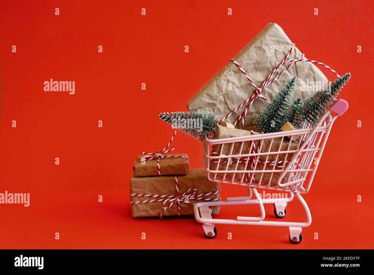 Vendita di Natale - Carrello e regali di Natale su sfondo rosso. Buon Natale, buon anno shopping concetto. Vista dall'alto e spazio di copia. Foto Stock
