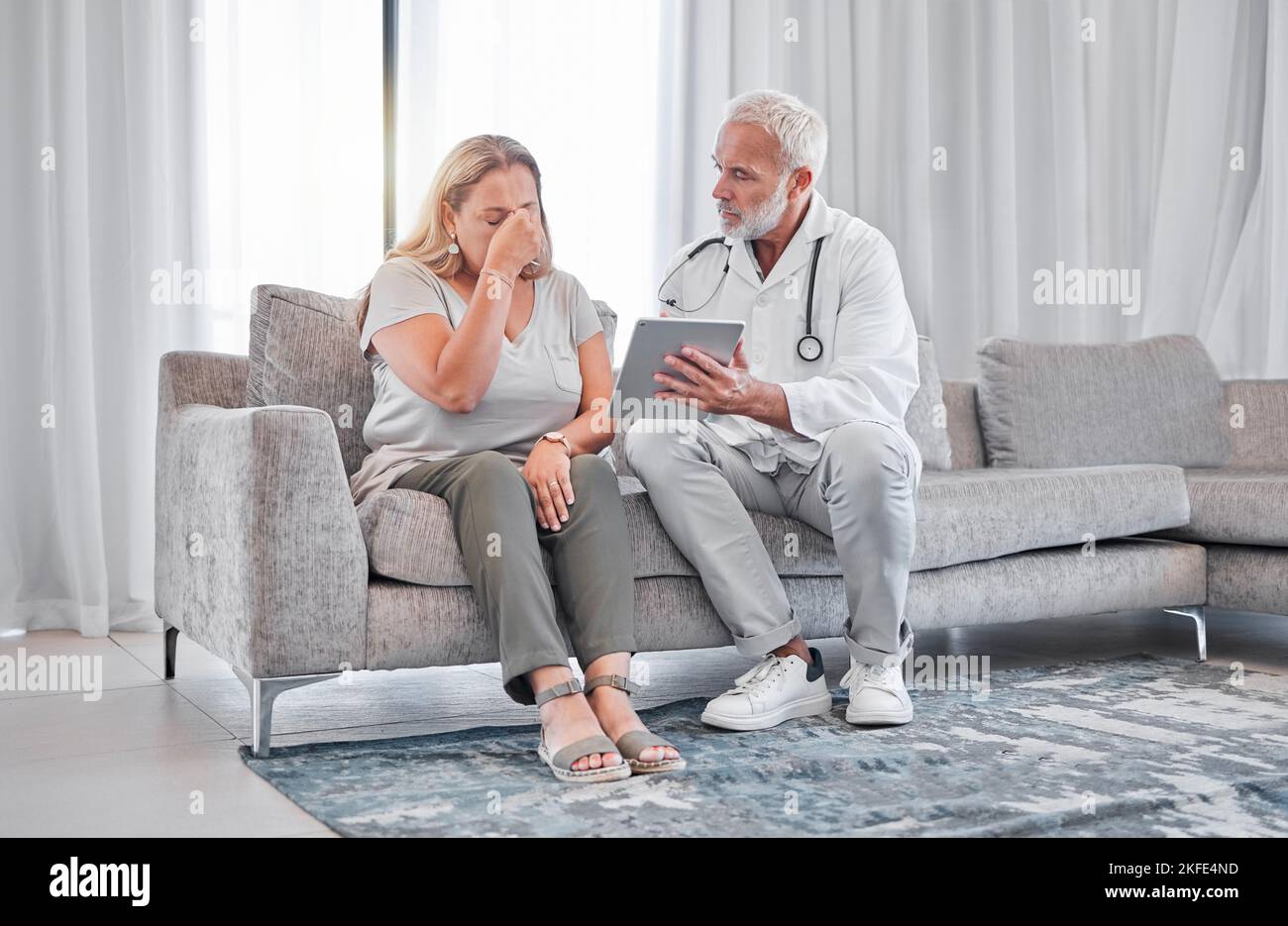 Medico, tablet e cattive notizie con una paziente donna nel salotto di casa sua con un medico. Assistenza sanitaria, assicurazione e cancro Foto Stock