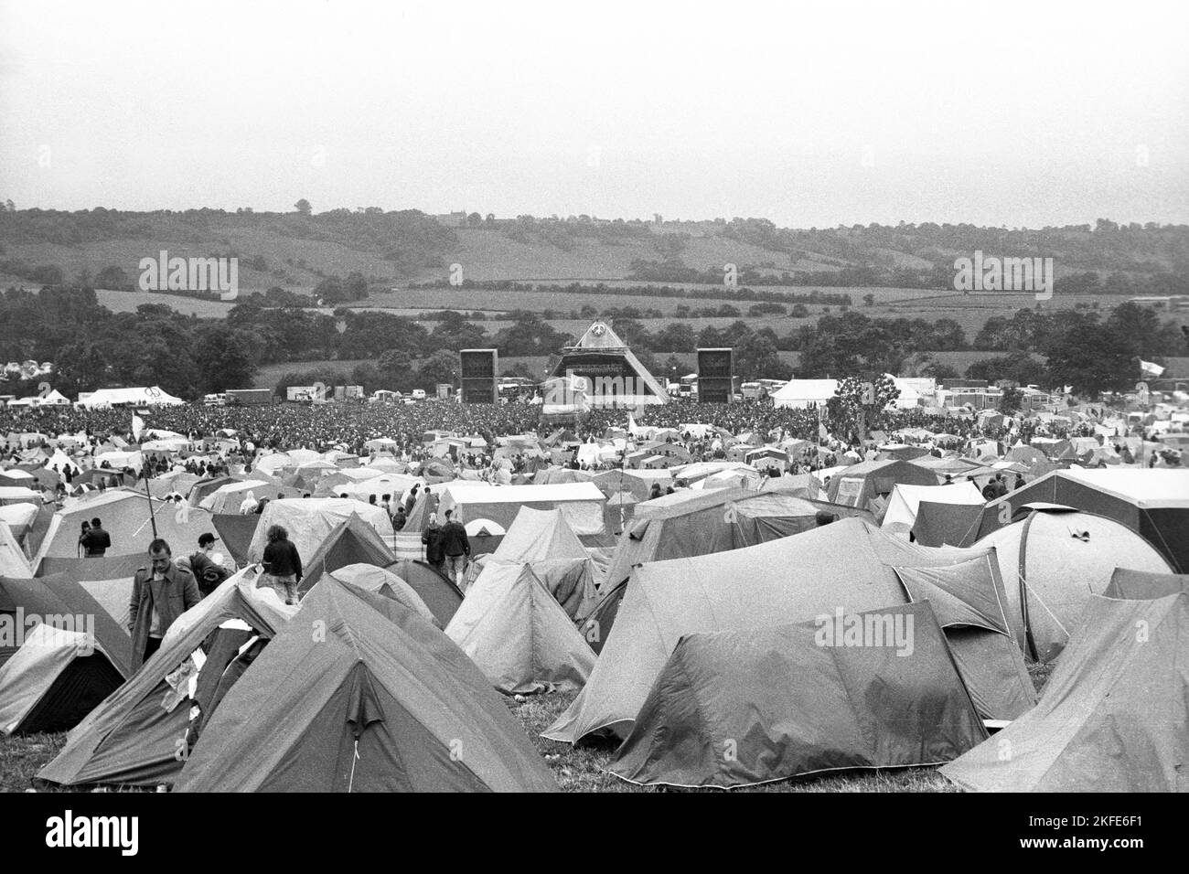 GLASTONBURY 1990, CAMPO PRINCIPALE, AMPIA VISTA: La vista dal retro del campo principale attraverso le tende e i camper verso il Pyramid Main Stage al Glastonbury Festival, Pilton Farm, Somerset, Inghilterra, giugno 1990. Nel 1990 il festival ha celebrato il suo ventesimo anniversario. A questo punto si poteva ancora accamparsi in fondo al campo principale. Non consentono più le tende sul retro del campo principale. Fotografia: ROB WATKINS Foto Stock
