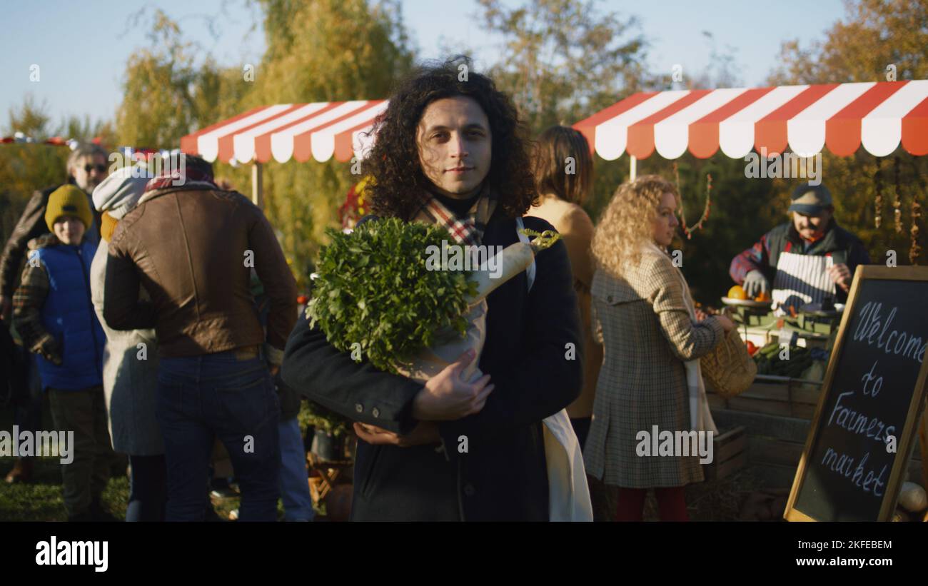 L'uomo riccio di mezza età che si posa con una borsa di verdure o frutta e guarda la macchina fotografica, si prende cura della sua salute acquistando prodotti vegetariani, biologici e sani. Foto Stock