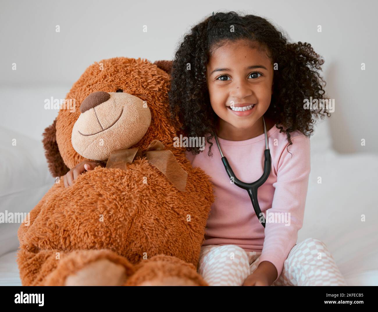 Stetoscopio, orsacchiotto e ragazza con un bambino il suo animale farcito con un sorriso in casa sua. Ritratto di femmina felice con un giocattolo soffice Foto Stock