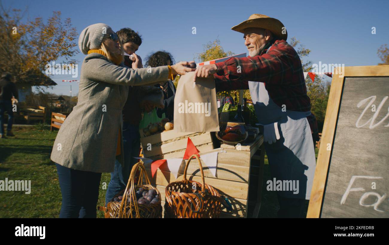 La gente che acquista, scegliendo frutta e verdura al mercato agricolo locale, imballando le merci in sacchetti ecologici. Fiera autunnale nei fine settimana all'aperto. Cibo vegetariano e biologico. Agricoltura. Sistema dei punti vendita. Foto Stock