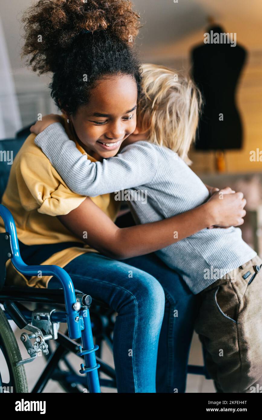 Bambina nera con disabilità in sedia a rotelle abbracciata con il fratello minore. Foto Stock