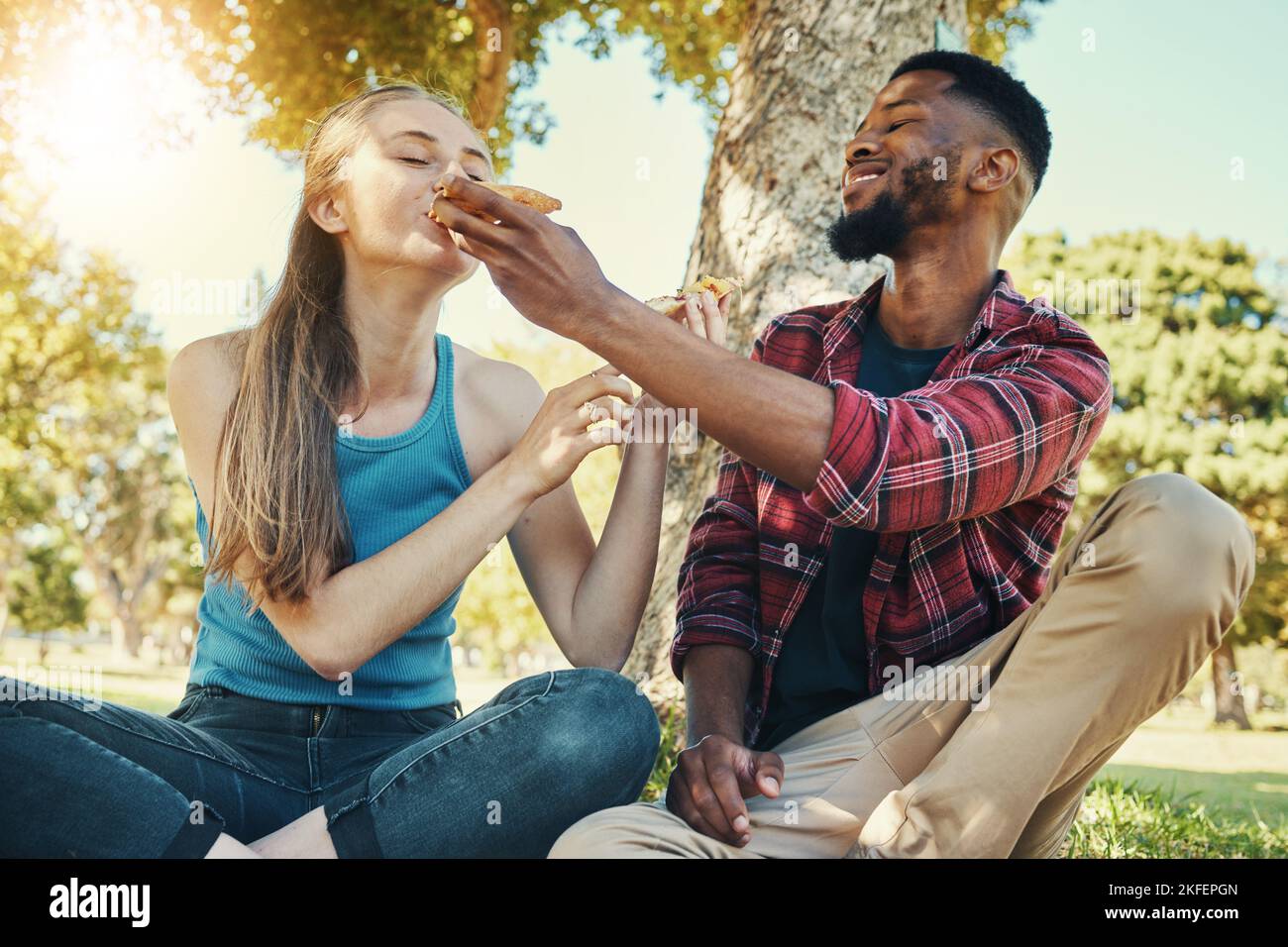 Pizza, cibo e pic-nic con una coppia diversità in un parco durante l'estate per un appuntamento romantico insieme. Fast food, mangiare e amare con un uomo e una donna Foto Stock