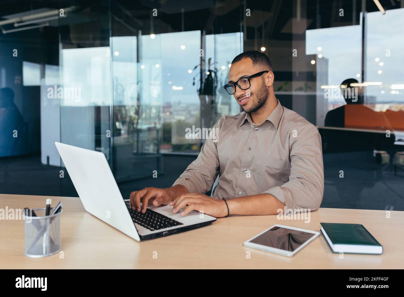 Programmatore afro-americano al lavoro con computer portatile all'interno dell'ufficio, uomo in occhiali e codice di scrittura casuale per i programmi. Foto Stock