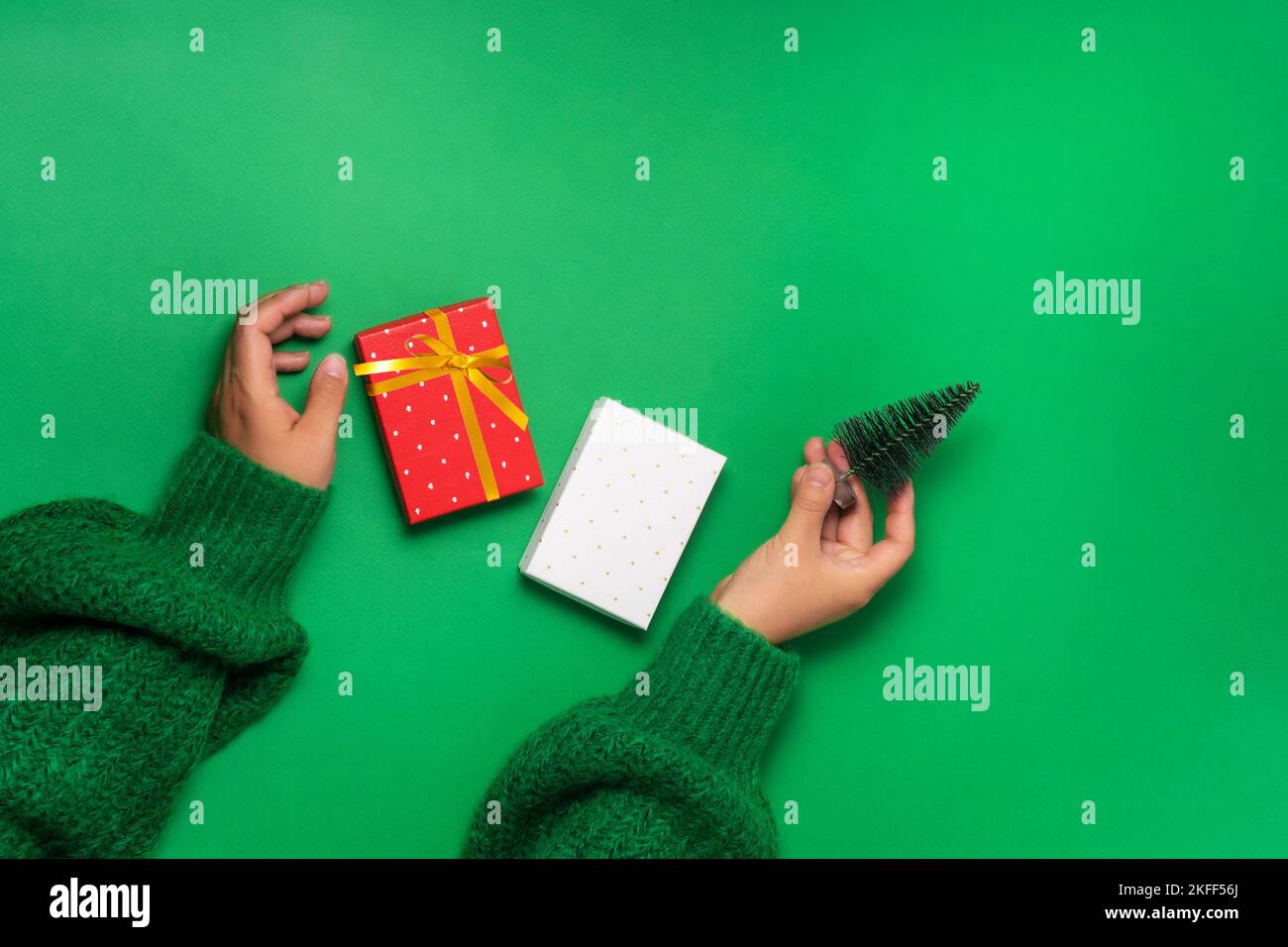 Mani della donna che tengono levitating scatole del regalo e albero decorativo di natale, vista superiore sfondo verde. Concetto di preparazione dei regali di Natale Foto Stock