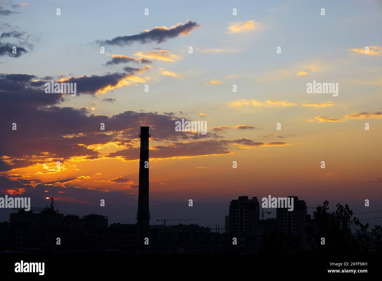 Profilo di alta torre di camino e gli edifici durante il tramonto con nuvole e colori drammatici. Foto Stock