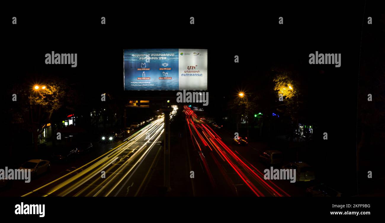 Yerevan, Armenia - 27 ottobre 2022: Sentieri leggeri da auto che passano da un banner pubblicitario di strada, che chiama a non inquinare l'ambiente con pl Foto Stock