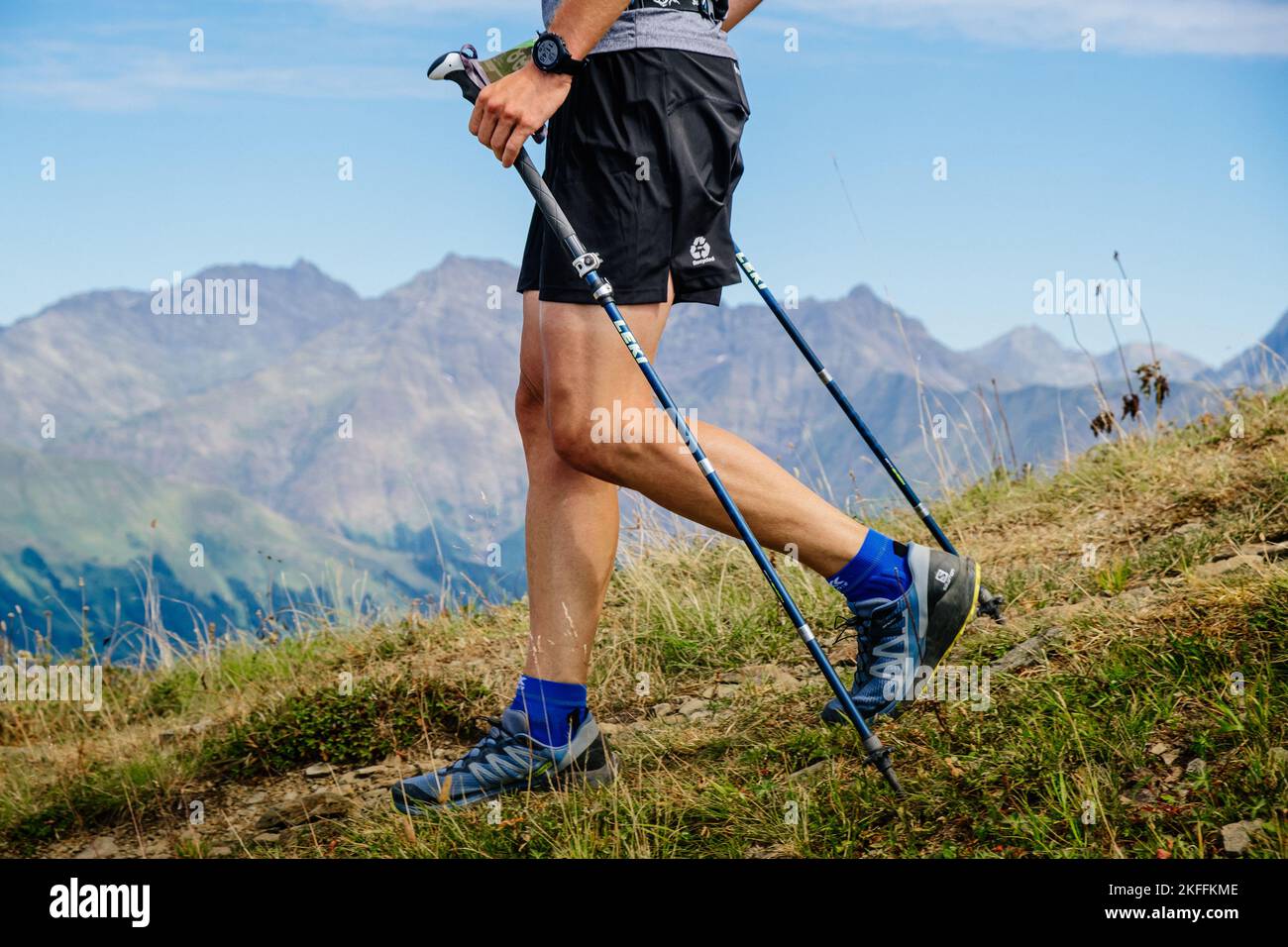 Rosa Khutor, Russia - 10 settembre 2022: Uomo gambe con bastoni da trekking discesa dalla montagna in Rosa Wild Trail Foto Stock
