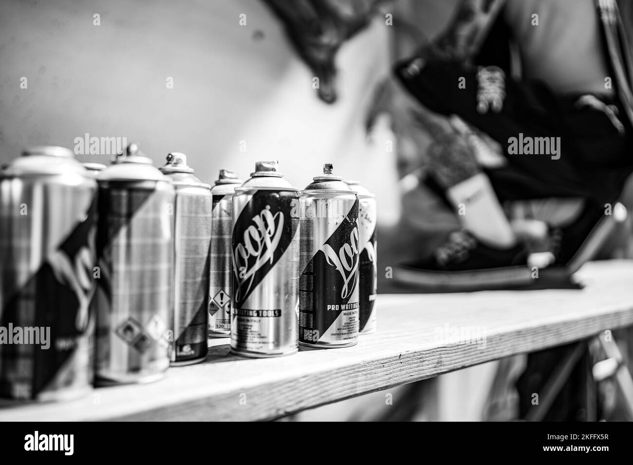 La vista in scala di grigi delle vernici spray su una superficie di legno vicino alla parete Foto Stock