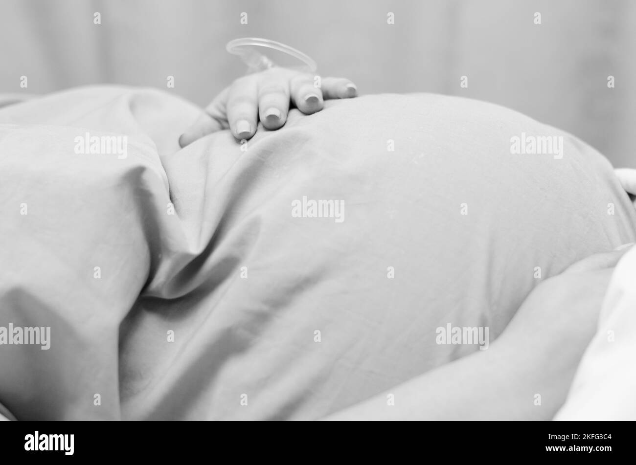 Una donna incinta in travaglio, sdraiata in un letto d'ospedale in attesa della nascita del bambino. Foto Stock