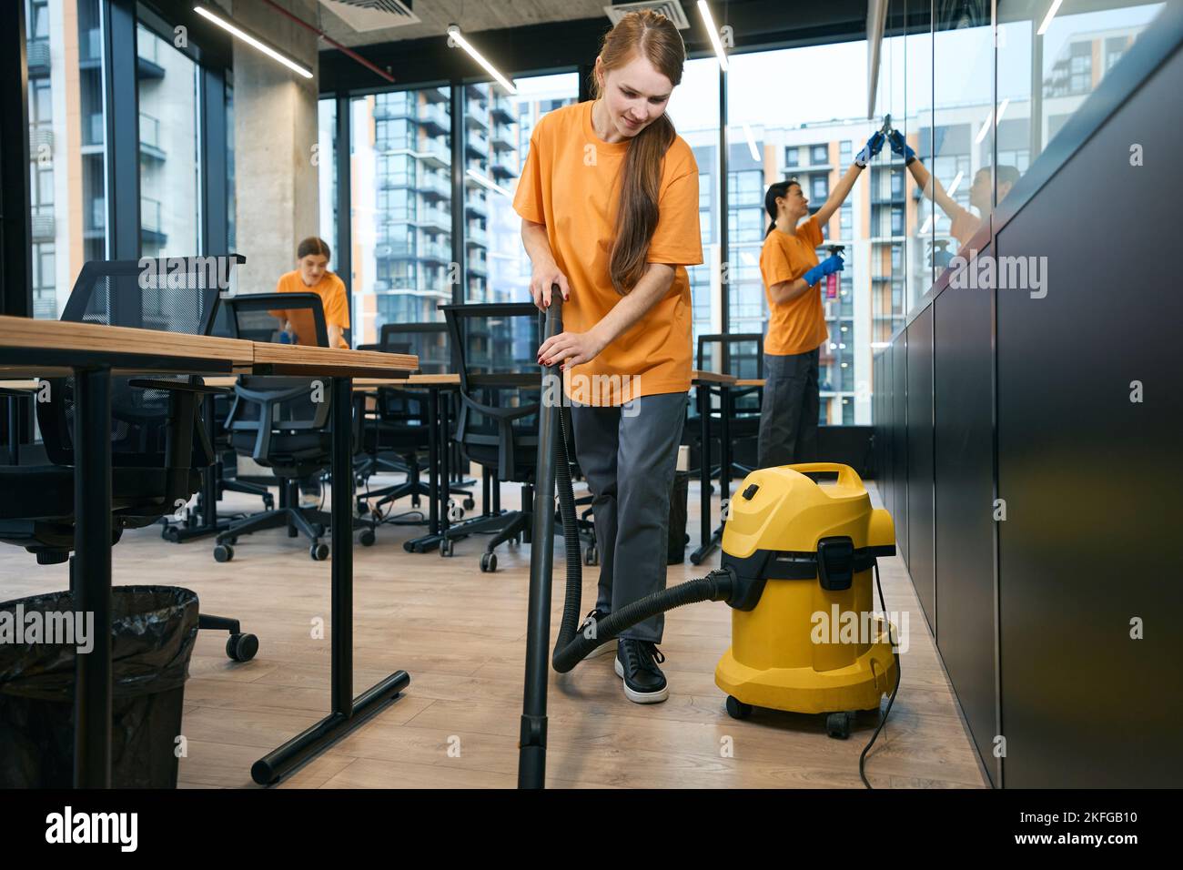 Il team di una società di pulizia femminile in tute pulisce e disinfetta lo spazio di coworking Foto Stock