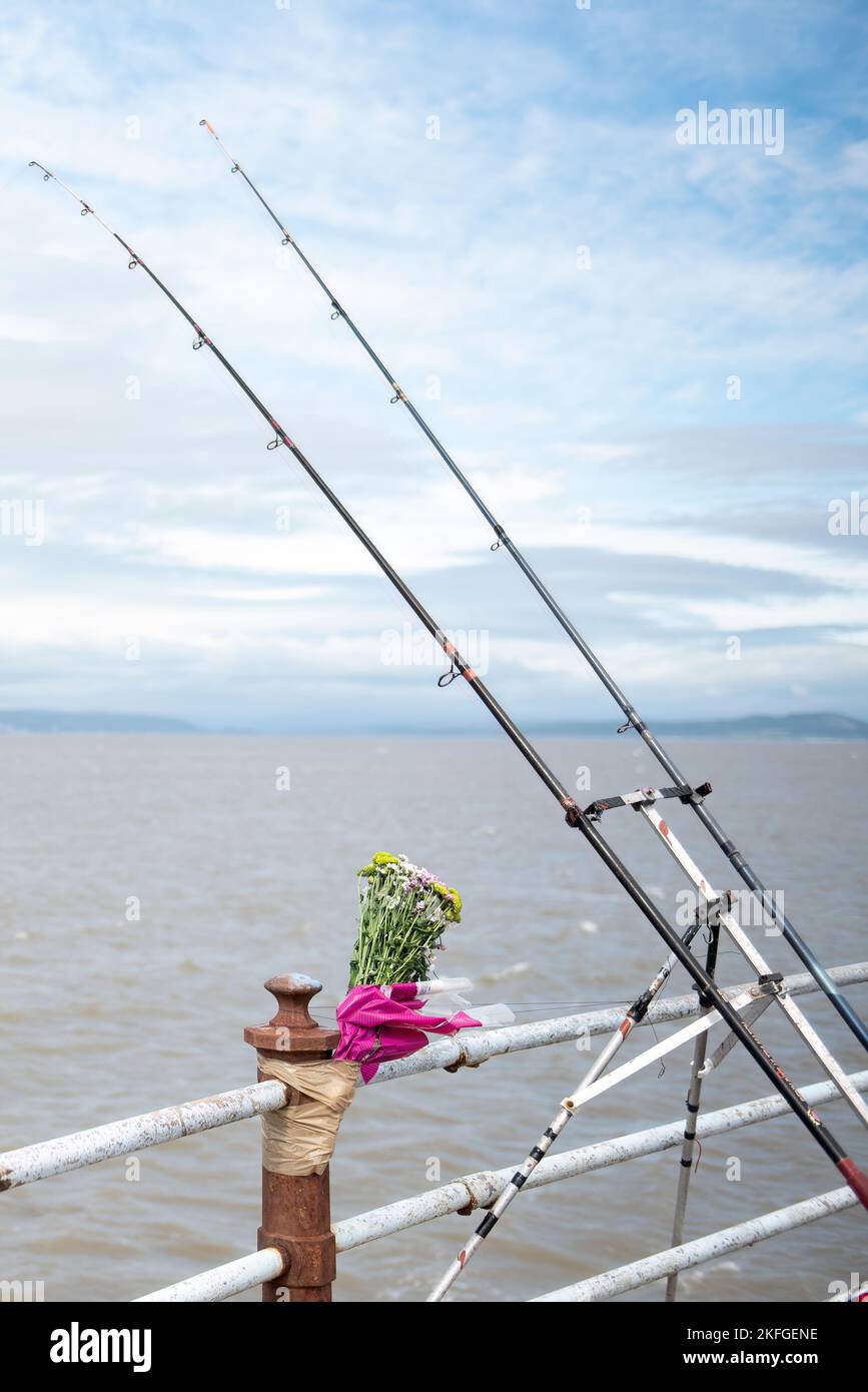Morecambe Bay di fronte al mare. Le canne da pesca si prestavano contro le ringhiere bianche con fiori commemorativi fissati sulle ringhiere dove le persone hanno perso la vita Foto Stock