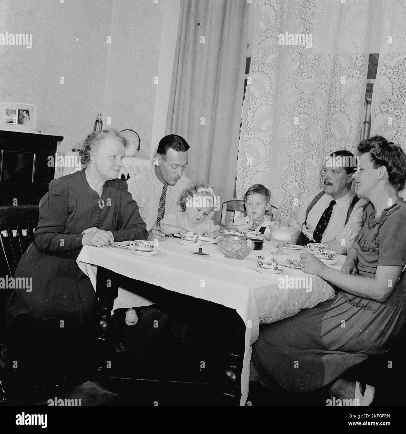 1950s, storia, vita familiare nel dopoguerra in Gran Bretagna, diverse generazioni si siedono intorno a un piccolo tavolo di legno coperto di stoffa con il tè insieme. Foto Stock