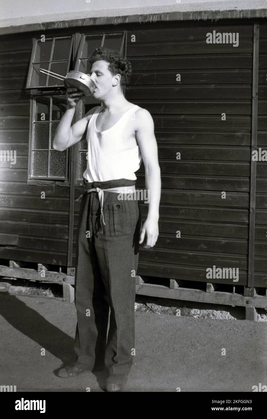 1949, storico, fuori dai suoi quartieri, una capanna, un uomo che beve da una padella di allumino metallico? RAF Longford Camp, Market Drayton, Inghilterra, Regno Unito Foto Stock