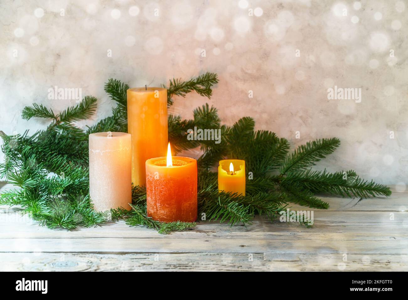 Secondo Avvento, sistemazione con quattro candele in arancione e giallo, due sono illuminate con una fiamma, rami di abete su legno rustico chiaro, bokeh fondo, copia Foto Stock