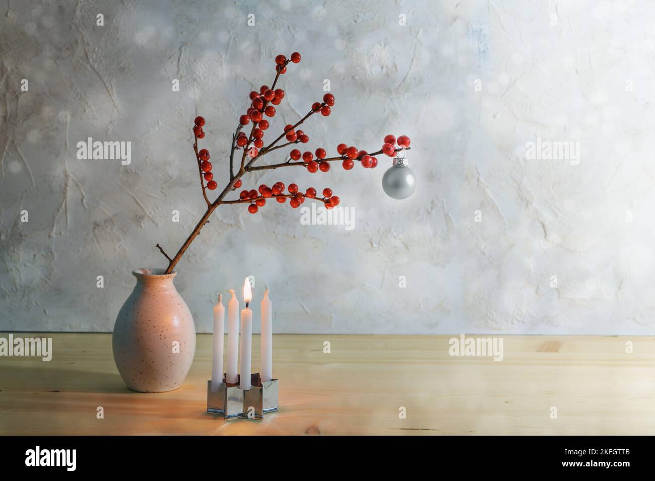 Primo avvento minimalista con quattro piccole candele, una è in fiamme e un ramo di bacche con una palla di natale in argento in un vaso, sfondo innevato con copia Foto Stock