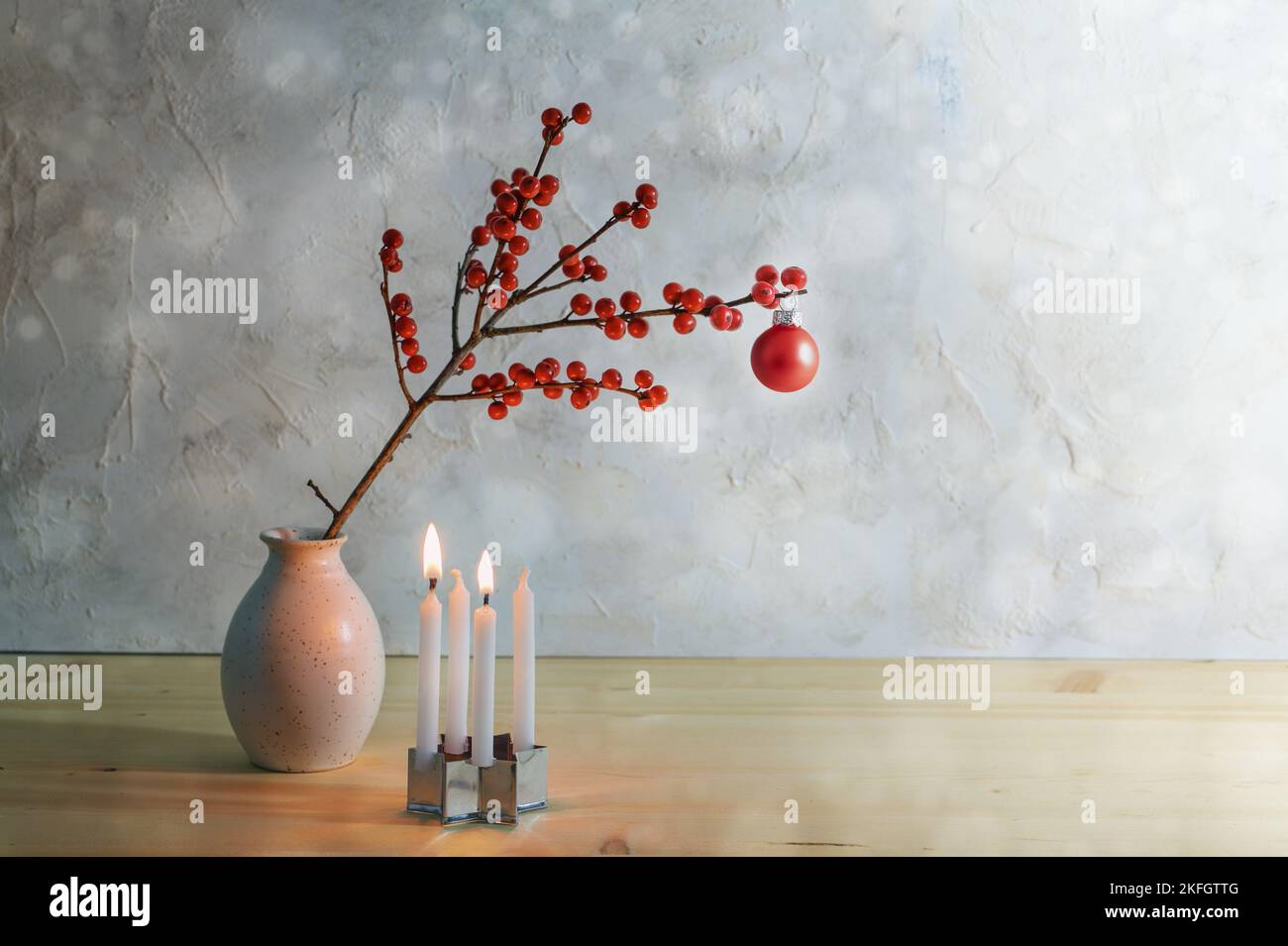 Secondo avvento minimalista con quattro piccole candele, due bruciano e un ramo di bacca con una palla di natale rossa in un vaso, sfondo innevato con copia Foto Stock
