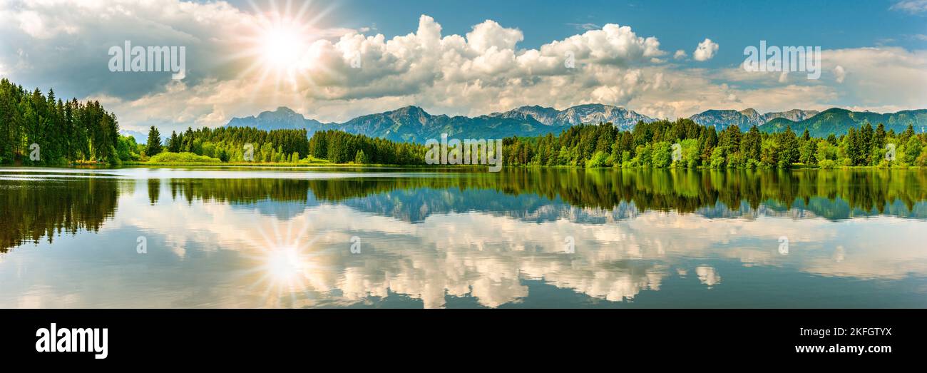 paesaggio panoramico con lago, catena montuosa e sole sul cielo Foto Stock
