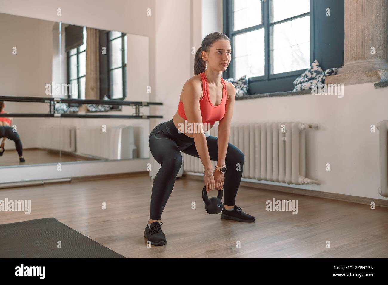 Una pesatrice femminile forte e muscolosa sta facendo squats con un kettlebell in una palestra. Foto Stock