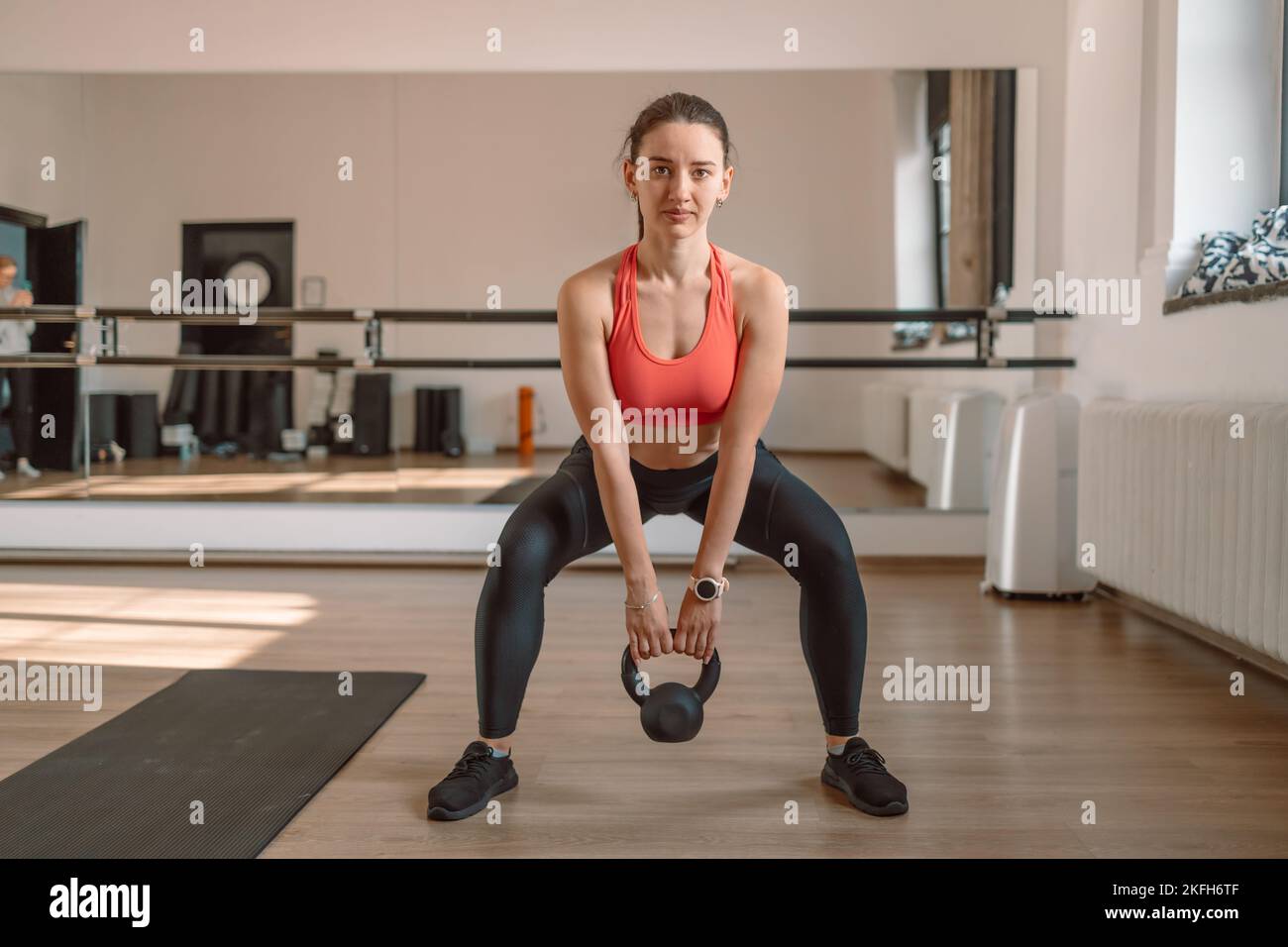 Una pesatrice femminile forte e muscolosa sta facendo squats con un kettlebell in una palestra. Foto Stock