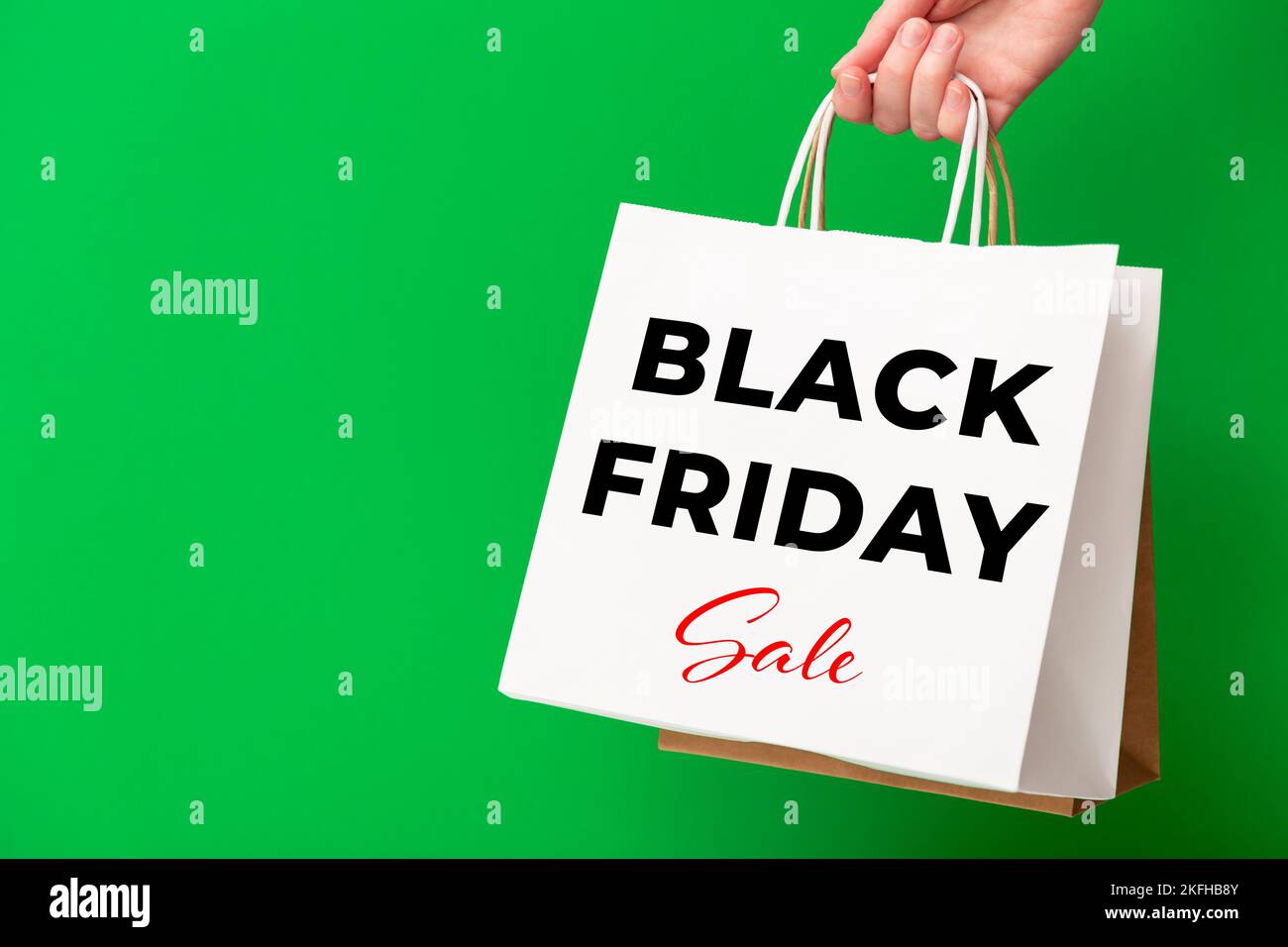 Mano femmina che tiene borse da shopping con Black Friday sale testo su sfondo verde. Vendita, sconto, concetto di shopping. Foto Stock
