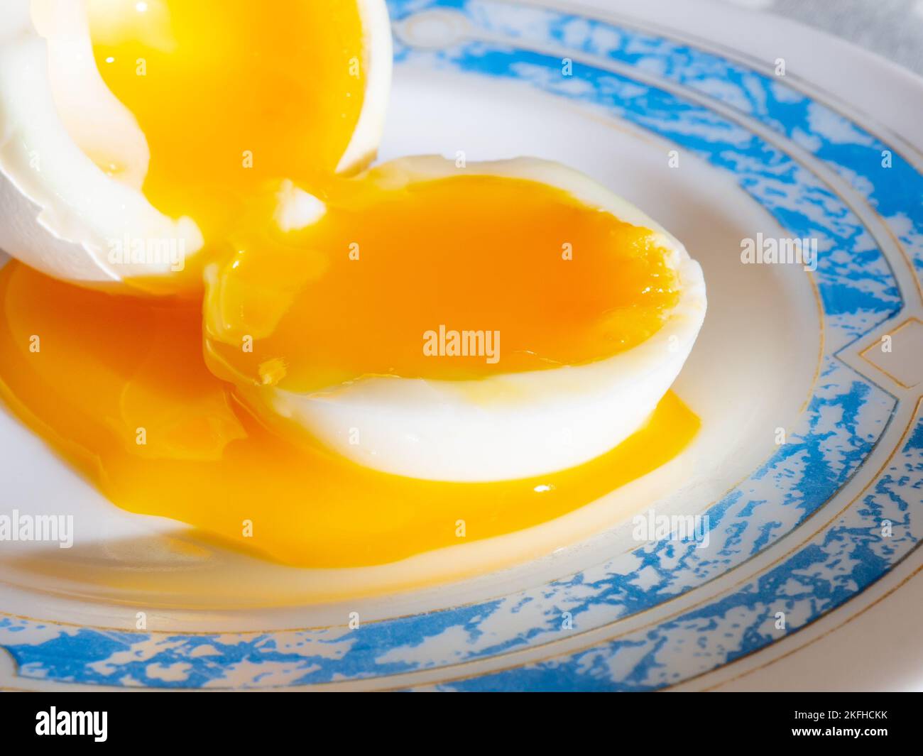 Primo piano di un uovo di pollo bollito su un piatto. Messa a fuoco selettiva. Il tuorlo d'uovo liquido si diffonde su un piatto. Foto Stock