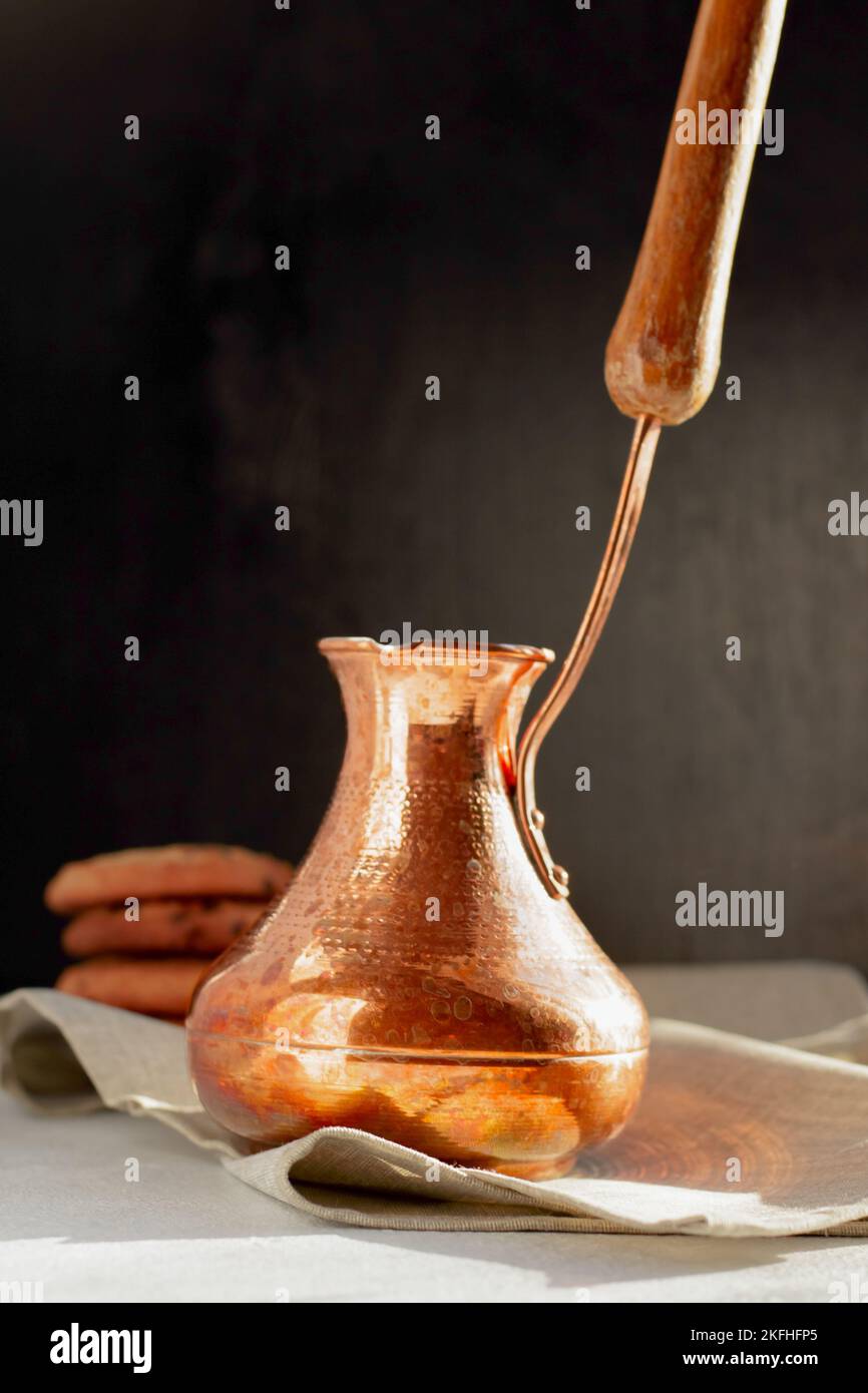 Vibrazioni mattutine. Caffè aromatico caldo in cezve turco, biscotti croccanti con gocce di cioccolato ai raggi del sole Foto Stock