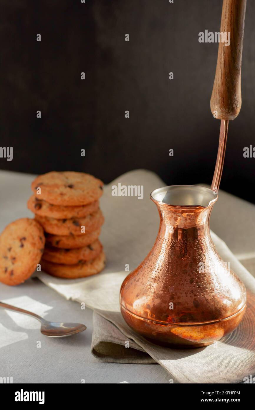 Vibrazioni mattutine. Caffè aromatico caldo in cezve turco, biscotti croccanti con gocce di cioccolato ai raggi del sole Foto Stock