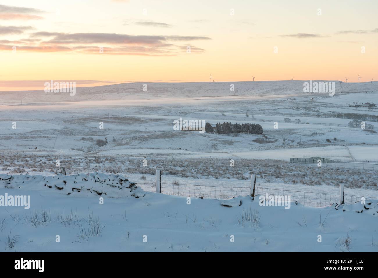 Il sole sorge sulla brughiera di Rossendale. Foschi fossati coperti di neve con turbine eoliche in lontananza. Bel cielo. Foto Stock