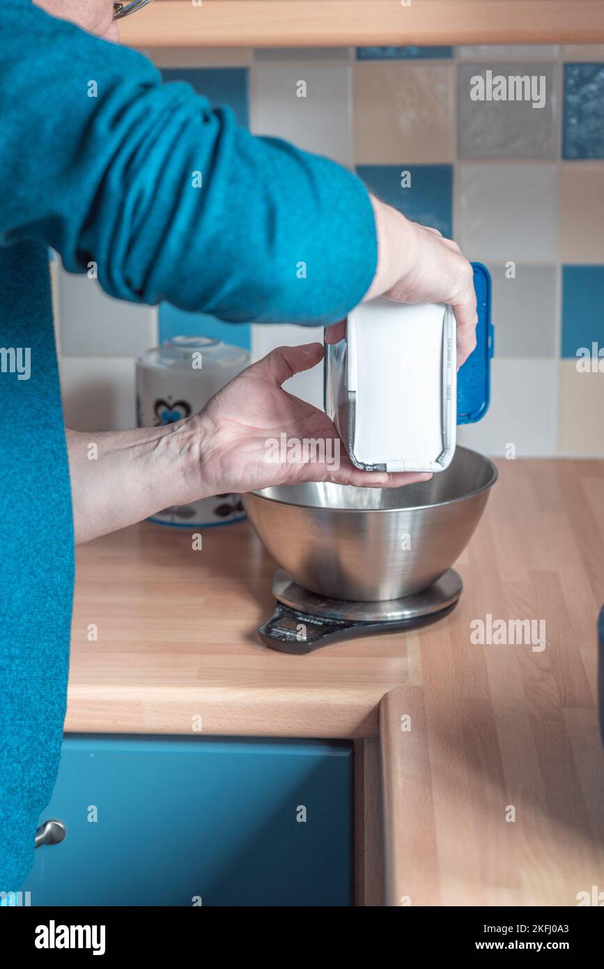 uomo che pesa la farina in cucina pesando bilance. Lato dell'uomo e mani visibili. Foto Stock