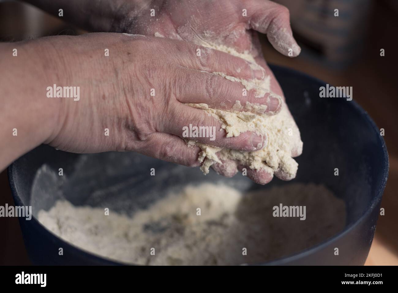 L'uomo usa le mani per unire la farina e il burro in un composto in un recipiente blu. Foto Stock