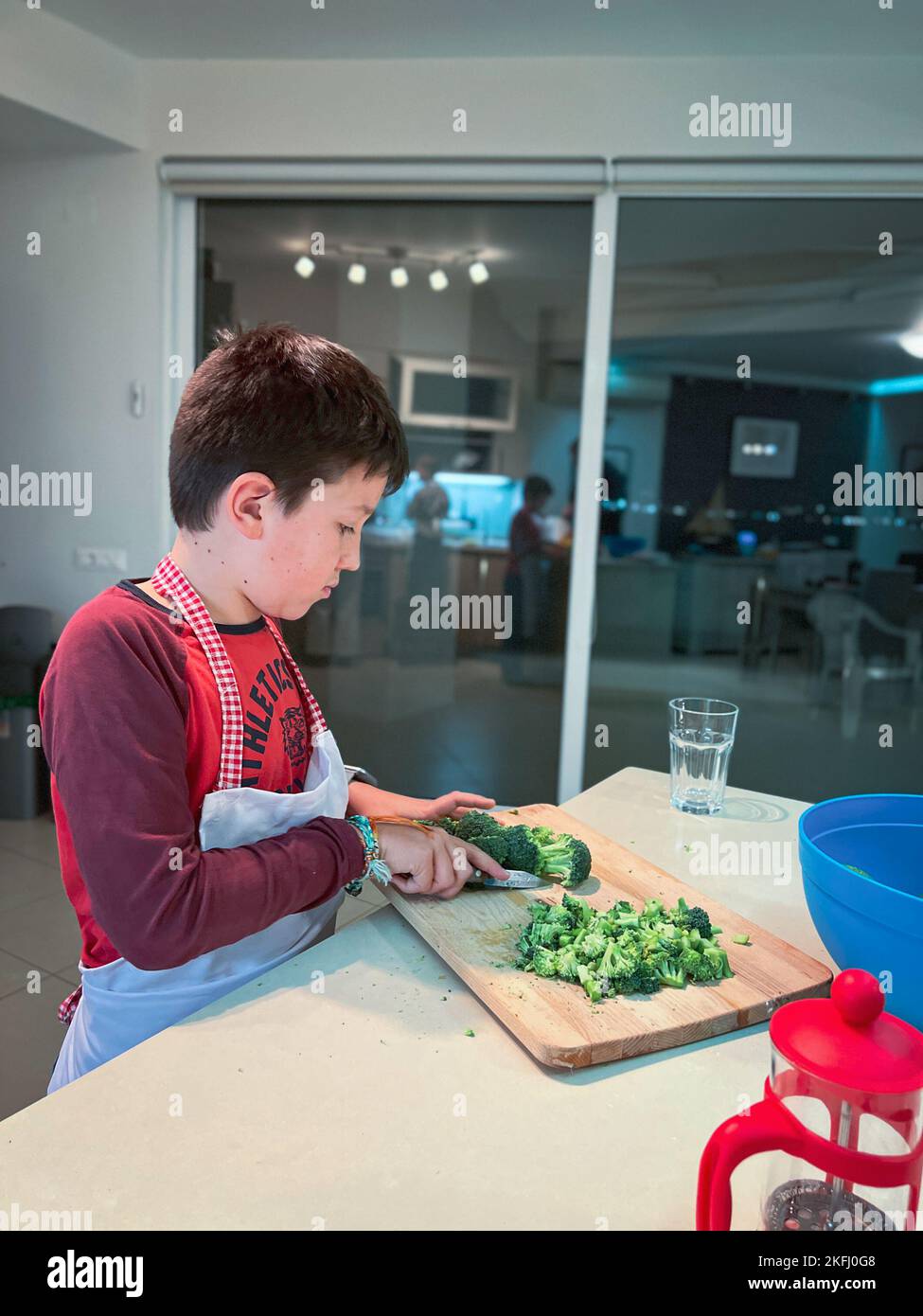 Vista laterale dell'adolescente caucasico che indossa un grembiule che taglia i broccoli sul tagliere in cucina a casa Foto Stock