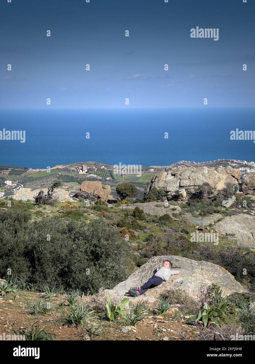 Ragazzo che si rilassa sulla formazione rocciosa sopra la montagna con idilliaca vista del mare in background nelle giornate di sole Foto Stock