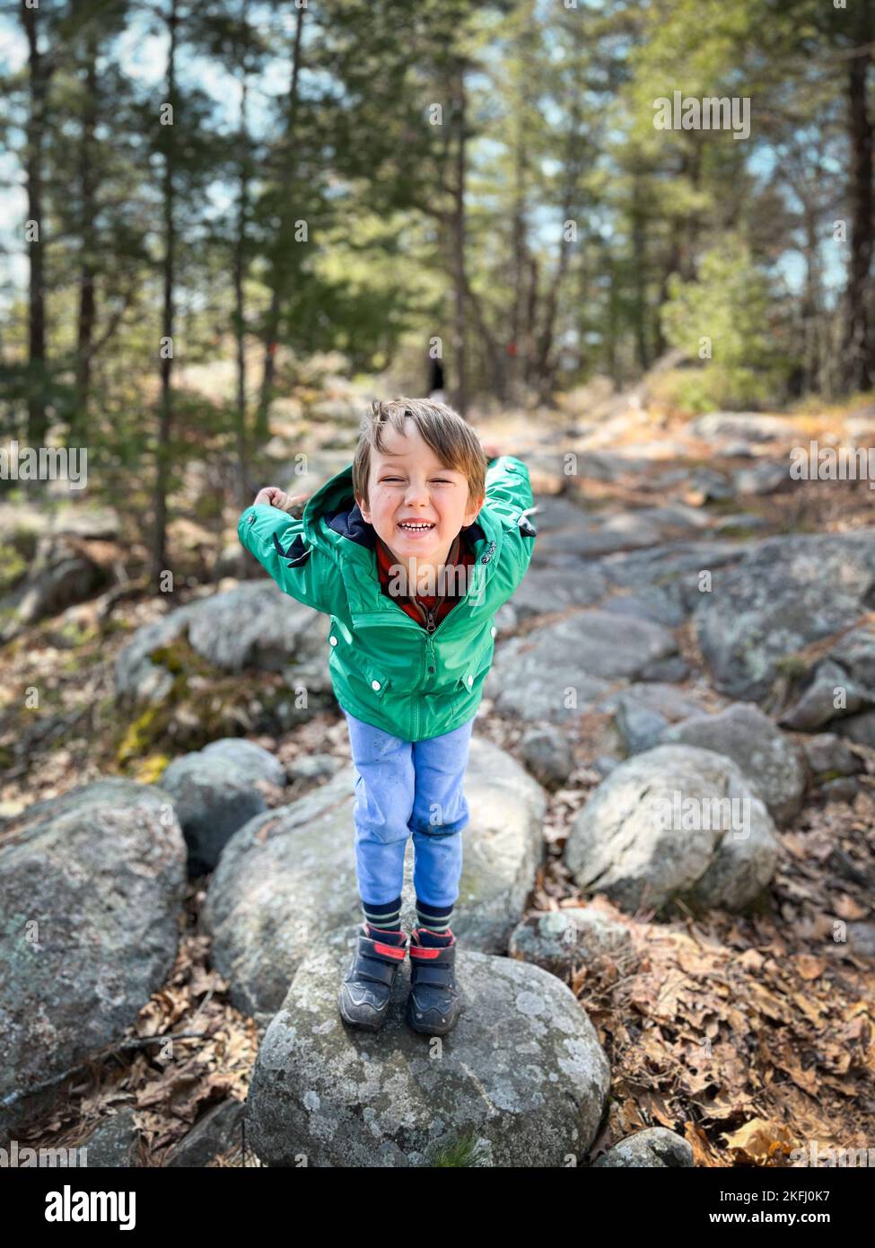 Ritratto di simpatico ragazzo che si piega e fa volti mentre si trova in piedi sulla roccia contro gli alberi nella foresta durante le vacanze Foto Stock