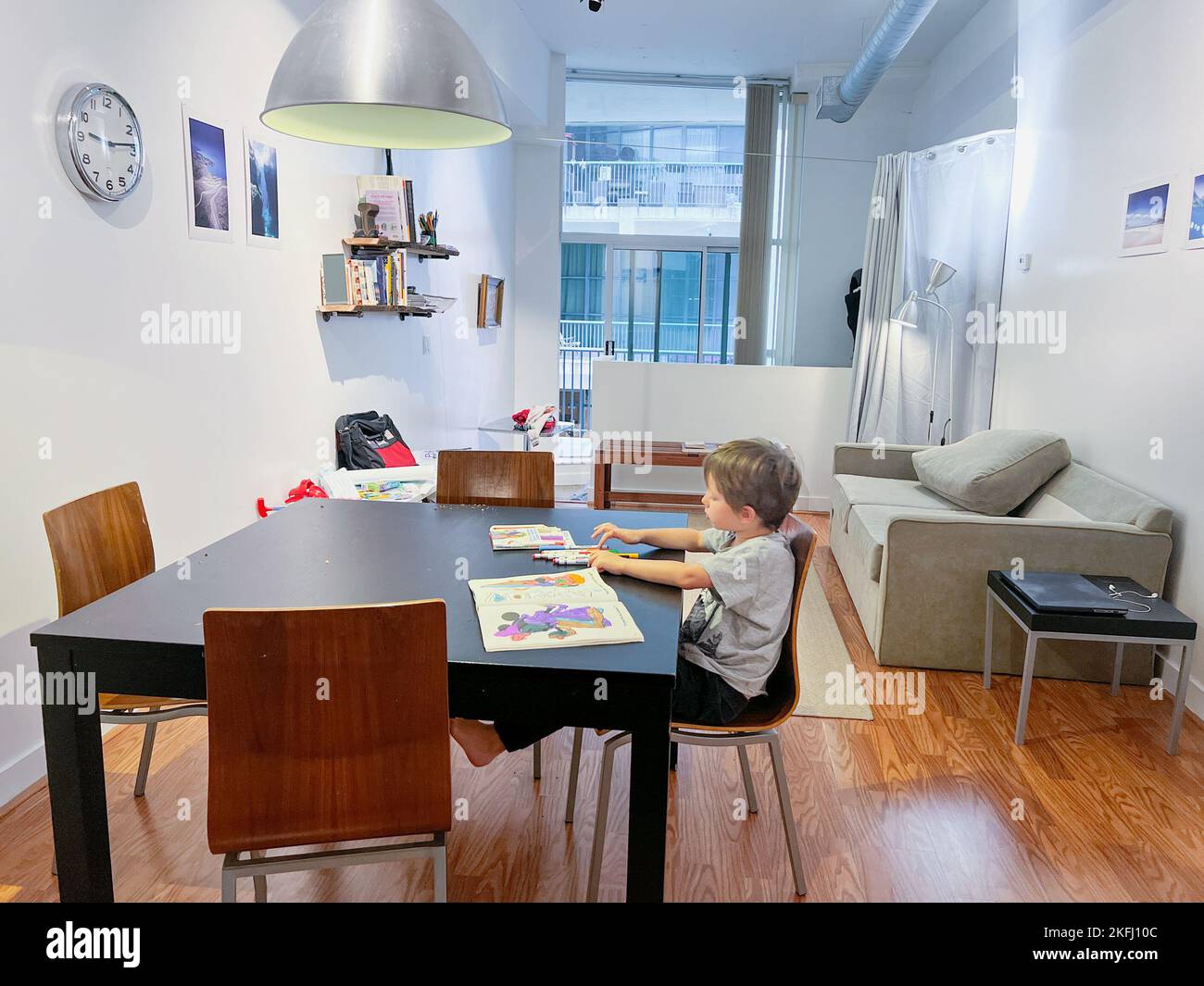 Ragazzo con matite colorate che disegnano nel libro mentre si siede sopra la sedia al tavolo da pranzo nel soggiorno a casa Foto Stock