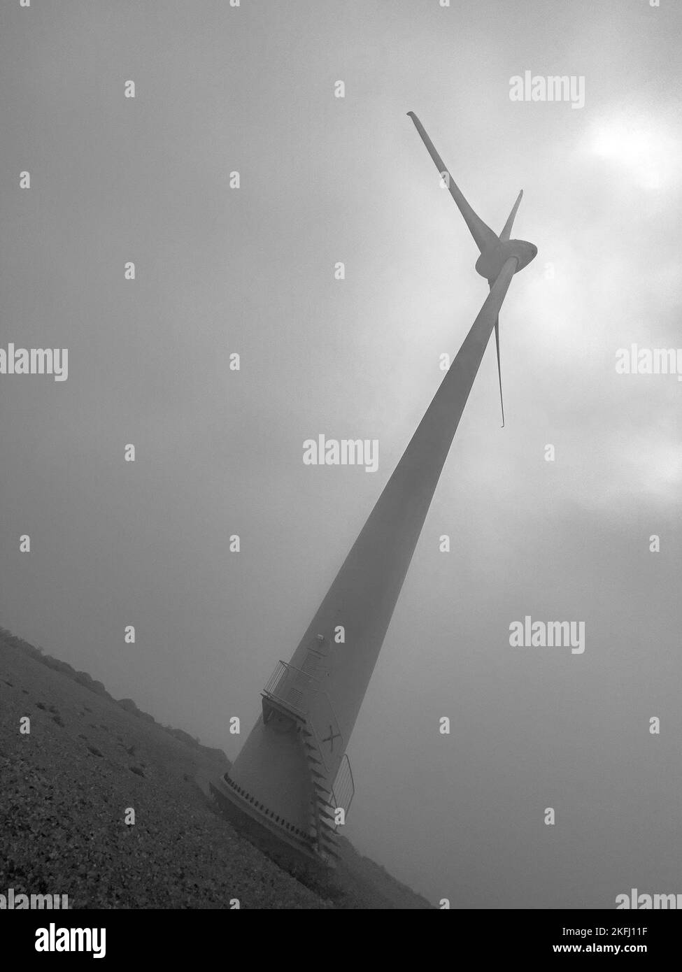 Vista dall'angolo basso di una turbina eolica alta in collina contro il cielo nuvoloso durante le giornate di sole Foto Stock