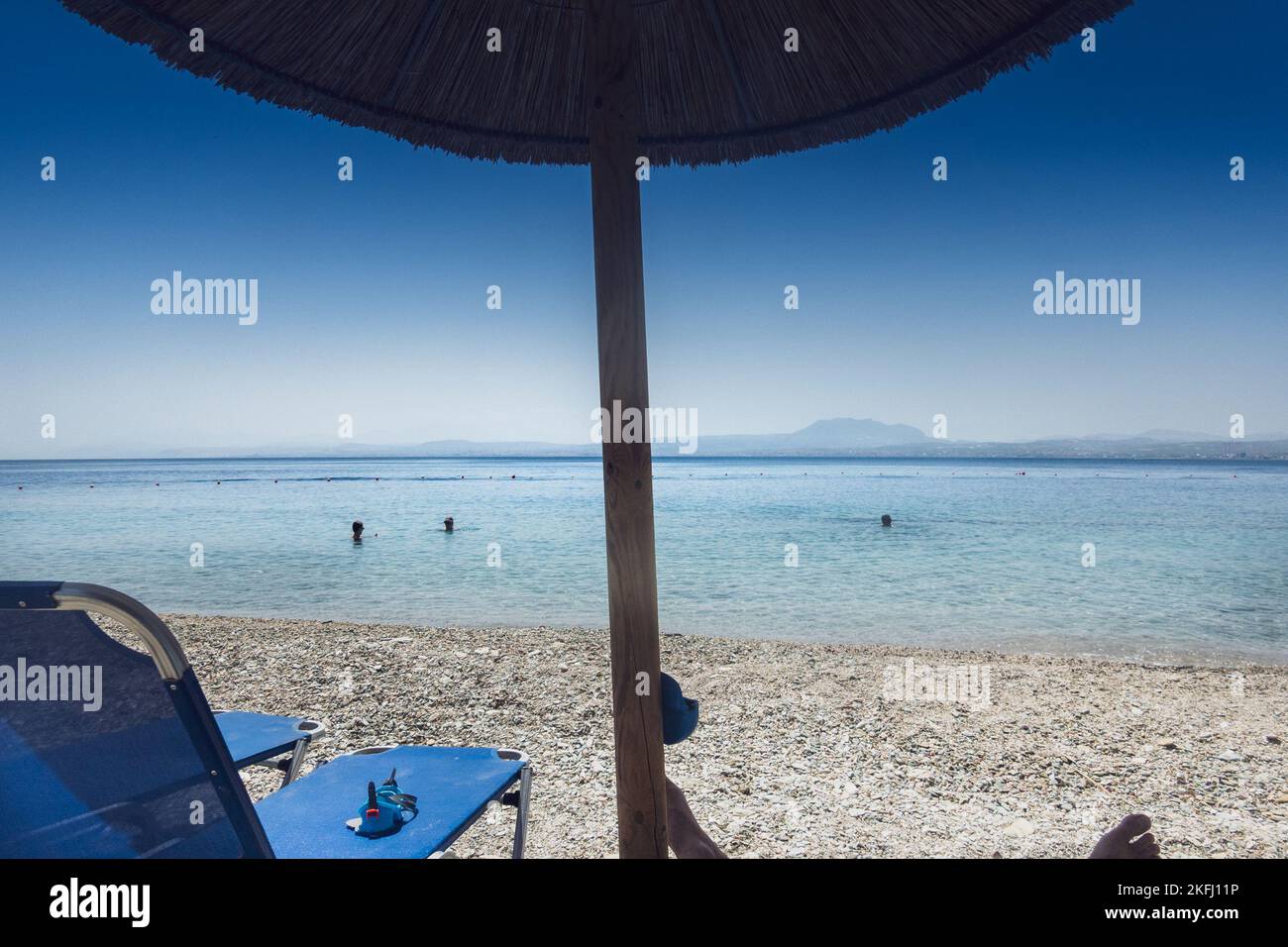 Sedie a sdraio con ombrellone in paglia in spiaggia e vista panoramica della calma del mare contro il cielo blu chiaro durante le giornate di sole Foto Stock