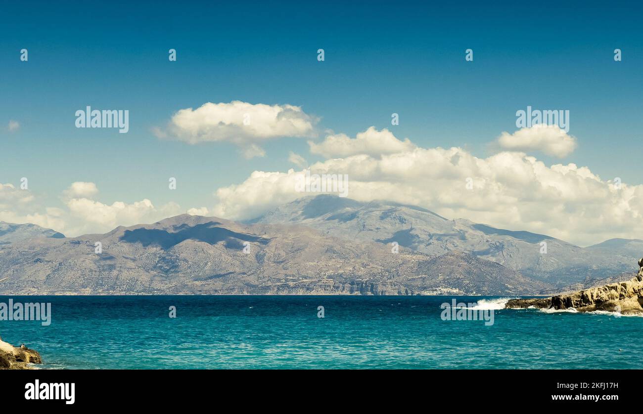Vista panoramica del mare blu e della montagna innevata contro il cielo nuvoloso durante le giornate di sole Foto Stock