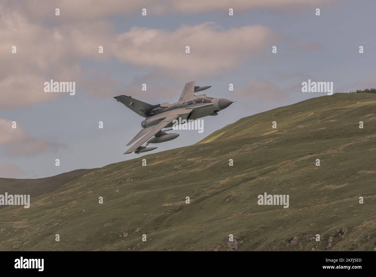 Aereo da combattimento militare che vola molto basso e veloce attraverso il circuito Mach in Galles. Colline sullo sfondo. Foto Stock