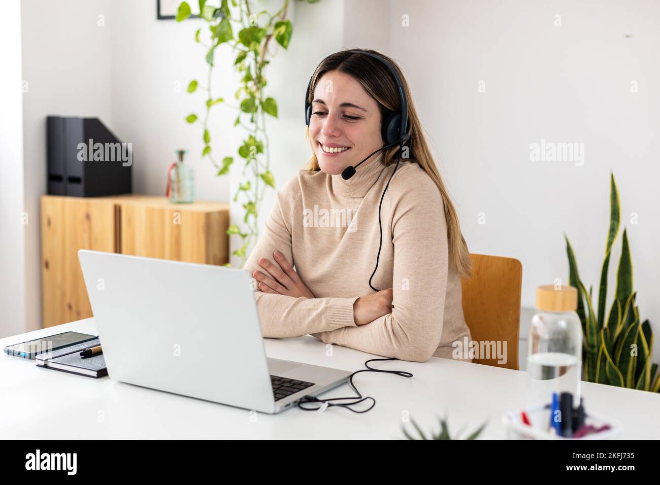 Giovane donna adulta in viaggio d'affari con cuffie che lavorano sul computer portatile in ufficio Foto Stock