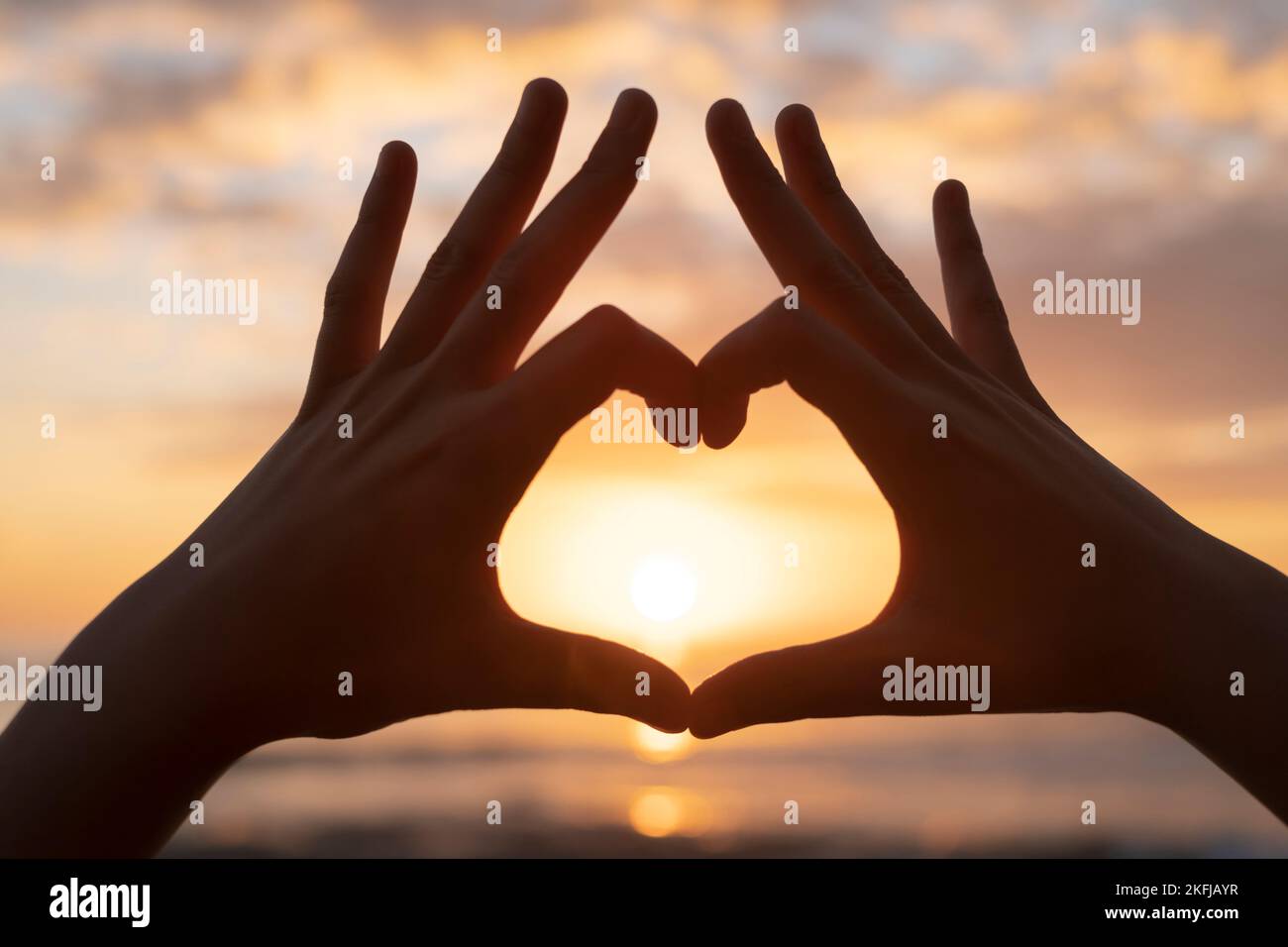 Donna mani silhouette fare cuore gesto simbolo sul mare tramonto sfondo, amore segno emozione Foto Stock