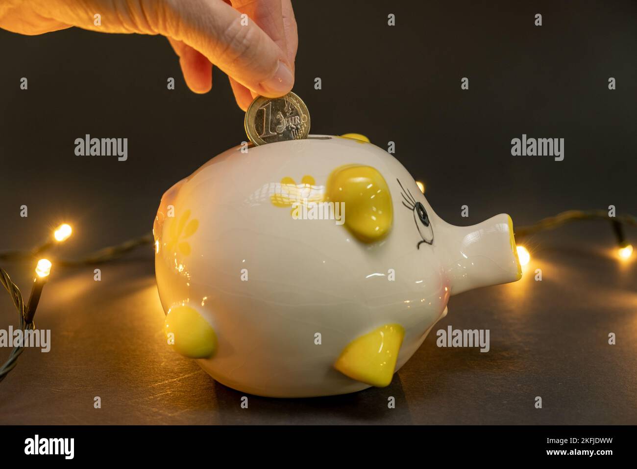 Mettere una moneta in maialino, su sfondo scuro con piccole luci a LED. Concetto di risparmio di denaro. spazio di copia. Foto Stock